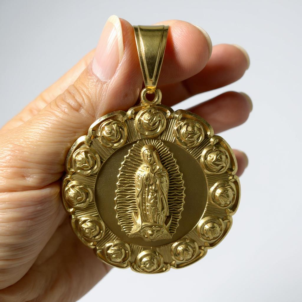 Gold plated pendant with religious figure of a Virgin Mary held by a hand against a white background