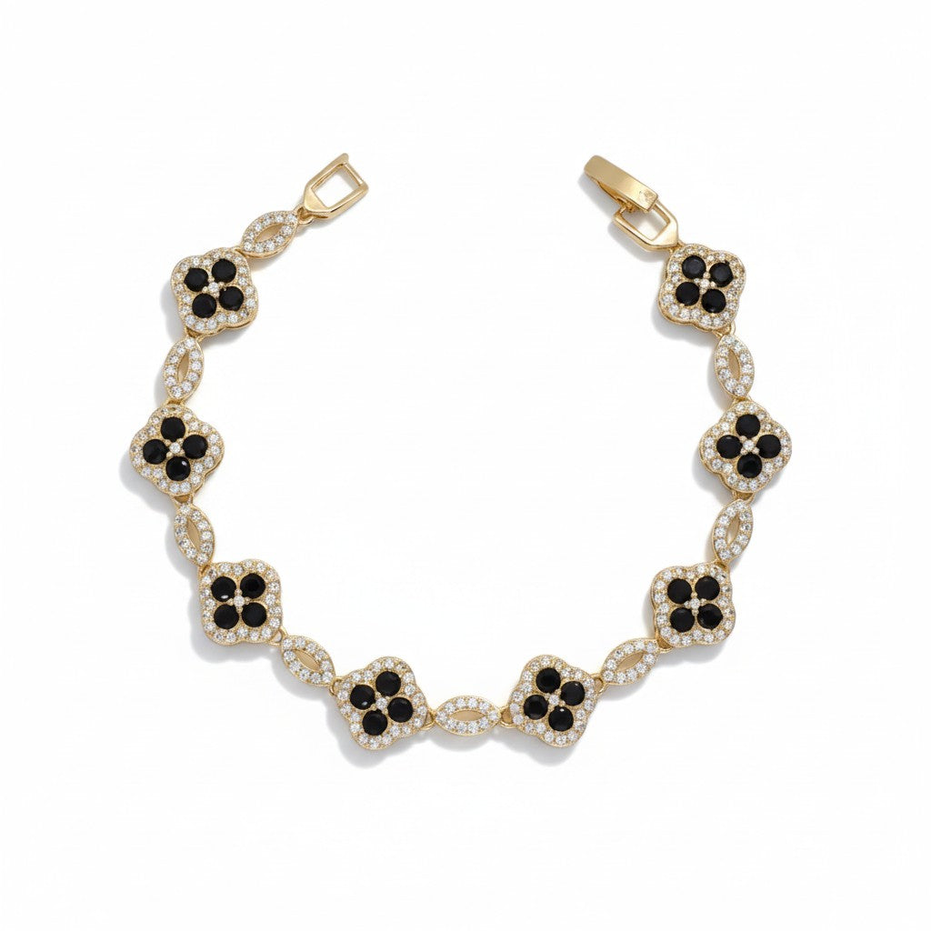 A gold-plated bracelet featuring a series of clover-shaped links, each adorned with a central cluster of round black stones surrounded by small clear stones, set against a plain white background.